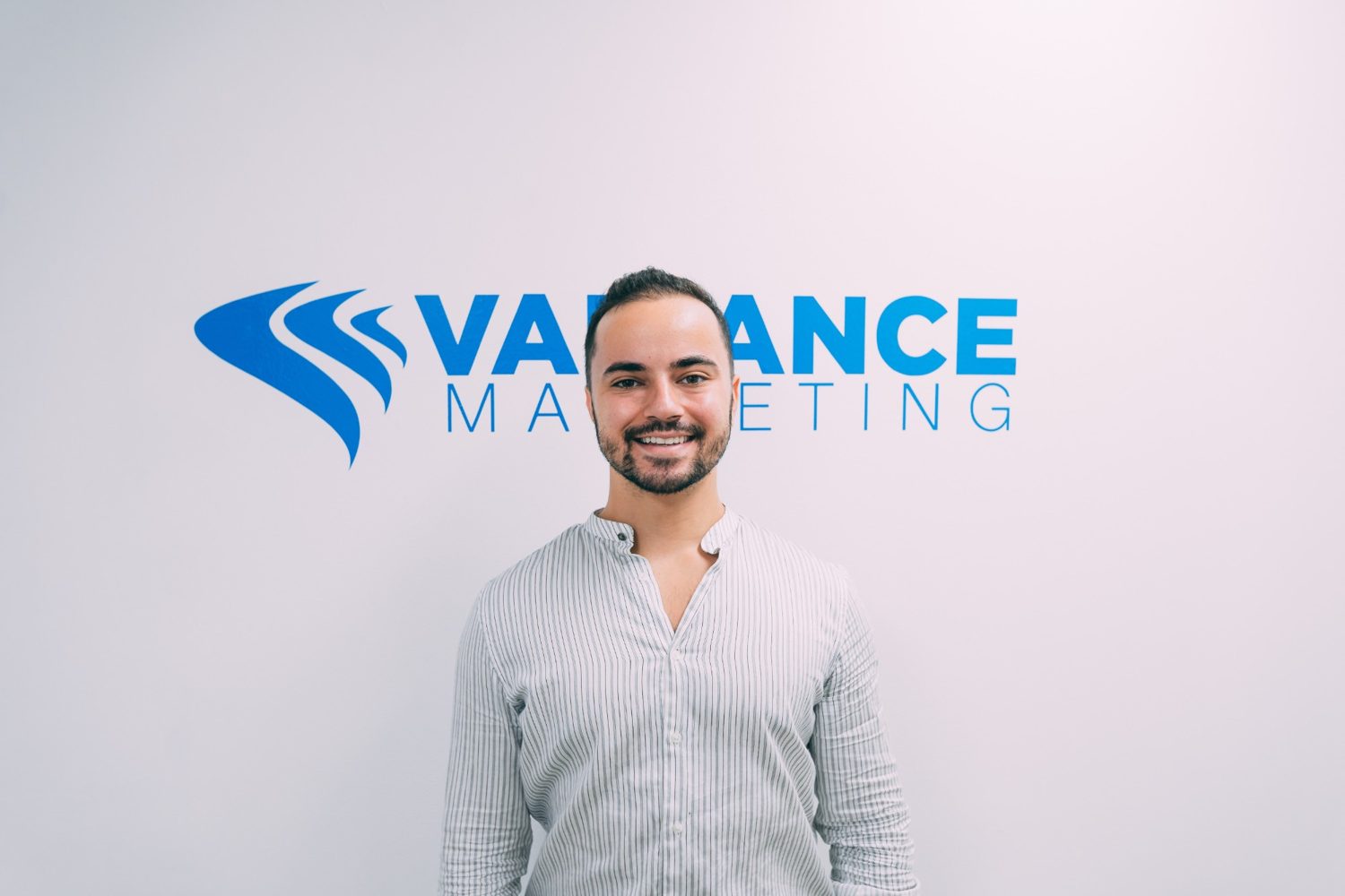 A Variance Marketing team member in front of the company logo wall